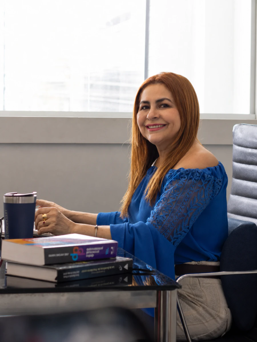 Dra. Mara Bittencourt sorrindo, trabalhando à mesa no escritório